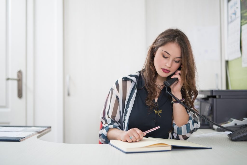 Portrait of young female secretary talking on the phone at her desk